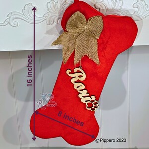 May include: Red dog bone-shaped Christmas stocking with a burlap bow and a wooden name tag that says "Rosie" with a paw print. The stocking is 16 inches tall and 8 inches wide.