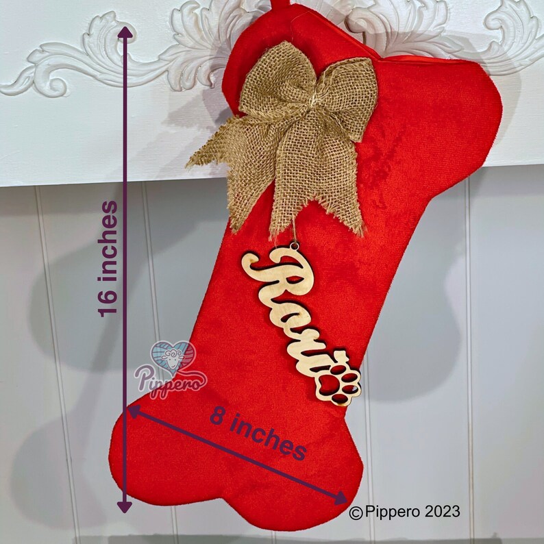 May include: Red dog bone-shaped Christmas stocking with a burlap bow and a wooden name tag that says "Rosie" with a paw print. The stocking is 16 inches tall and 8 inches wide.