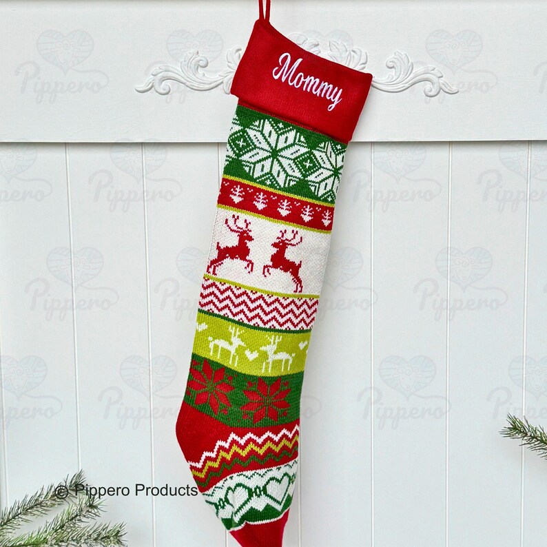 May include: Red and green Christmas stocking with a white snowflake pattern, reindeer, and a red poinsettia. The stocking has a red cuff with the word "Mommy" embroidered in white.