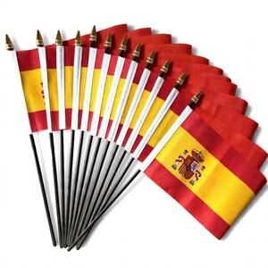 May include: A collection of twelve small handheld flags of Spain, each featuring horizontal red and yellow stripes with the national coat of arms centred on the yellow band. Each flag is attached to a white plastic pole topped with a gold finial.
