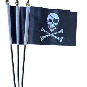 May include: A set of small pirate flags. Each flag is black with a white skull and crossbones design. The flags are attached to black poles with silver tips and white ribbon.