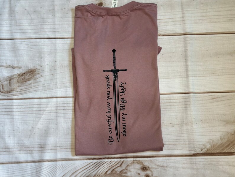 May include: A mauve t-shirt with a black sword graphic and the text "Be careful how you speak about my High Lady".