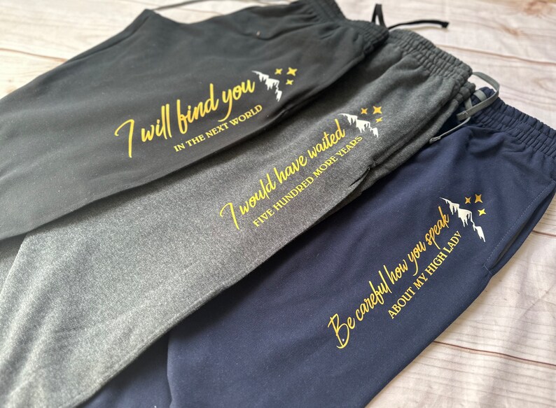 K&ouml;nnte beinhalten: Drei Jogginghosen in Anthrazit, Hellgrau und Marineblau. Jede Hose hat eine goldene Grafik und den Text: "I will find you in the next world", "I would have waited five hundred more years" und "Be careful how you speak about my high lady."