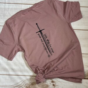 May include: A mauve t-shirt with a black sword graphic and the text "Be careful how you speak. Words have power." printed on the back.