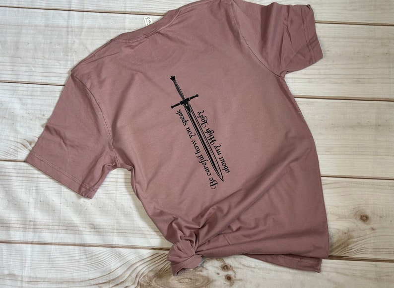 May include: A mauve t-shirt with a black sword graphic and the text "Be careful how you speak. Words have power." printed on the back.