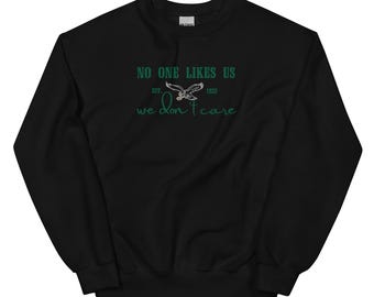 Może przedstawiać: Czarny sweter z zielonym tekstem, który brzmi "No one likes us, Est. 1833, We don't care". Zielony grafika orła znajduje się nad tekstem.