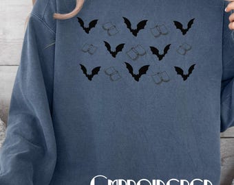 Puede incluir: Una sudadera azul grisáceo con un patrón de murciélagos y libros negros. La palabra "EMBROIDERED" está impresa en blanco en la parte inferior. La sudadera es de estilo casual.