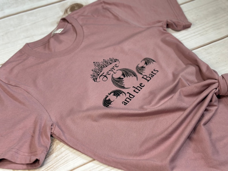 May include: A mauve t-shirt with a black graphic print of a crown with the text "Feyre and the Bats".