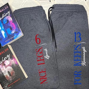 Puede incluir: Dos pares de pantalones de chándal grises con cinturilla con cordón. Un par tiene el texto "NICE LEGS. 6 Lynch" en rojo y blanco. El otro par tiene el texto "FOR KEEPS. 13 Kavanagh" en azul y blanco. También se ven dos libros.