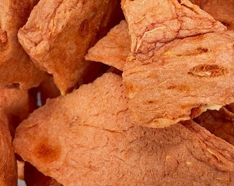 May include: Close-up of dried, reddish-orange fruit pieces. The pieces have a textured surface and irregular shapes, with some showing internal structures. The image suggests a healthy snack or ingredient.