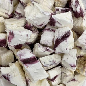 May include: Close-up of a pile of white, irregularly shaped pieces with streaks of dark purple throughout. The pieces appear to be a type of confection or food product, possibly a dessert or candy.