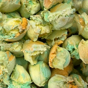 May include: A close-up of a pile of colorful, irregularly shaped, meringue cookies. The cookies are a mix of green, yellow, and orange.