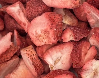 May include: Close-up of a pile of freeze-dried strawberry pieces. The pieces are a light pink color and have a slightly textured surface.