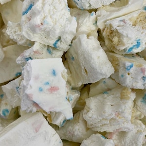 May include: Close-up of a pile of white, irregularly shaped confectionary pieces. The pieces have blue and pink speckles throughout. Some pieces have a light tan interior. The texture appears to be soft and crumbly.