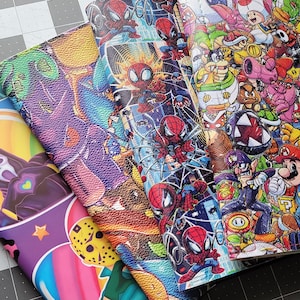 May include: Three different fabric swatches with colorful cartoon designs. The first swatch features a purple and blue graffiti-style design. The second swatch features a blue and orange design with a superhero theme. The third swatch features a multi-colored design with a video game theme.