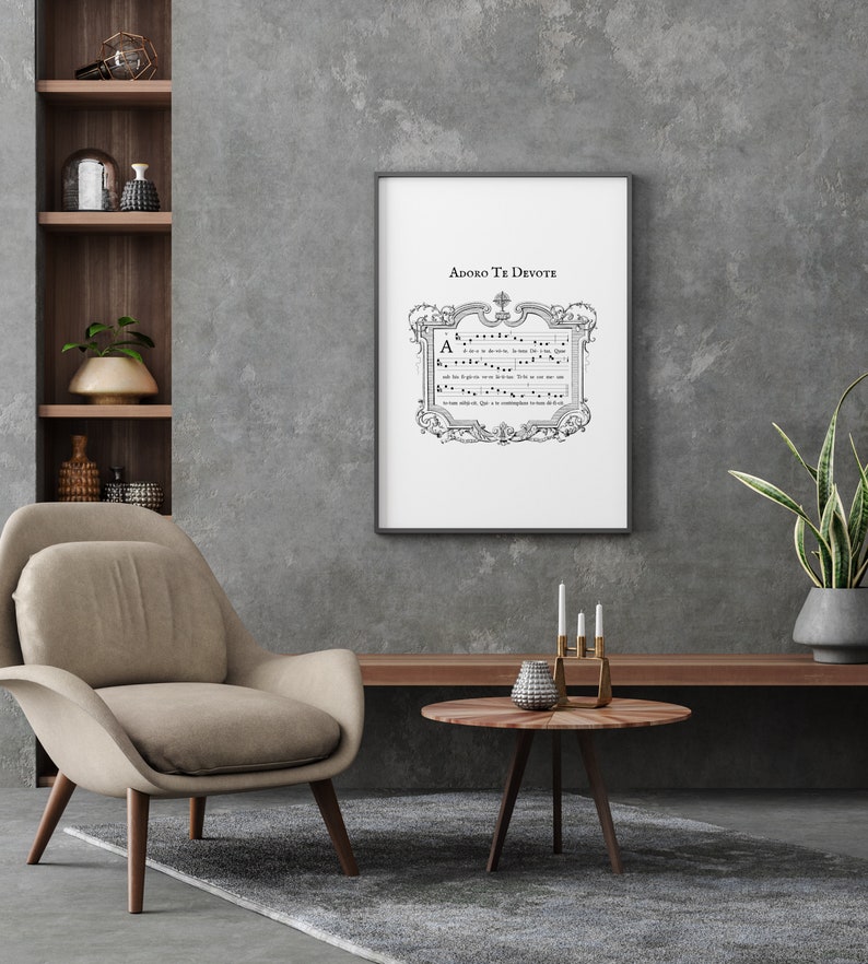 Puede incluir: Una impresi&oacute;n enmarcada de partituras con el t&iacute;tulo "Adoro Te Devote" en un marco negro sobre una pared gris. La impresi&oacute;n est&aacute; colgada sobre una mesa de madera con un jarr&oacute;n y velas.