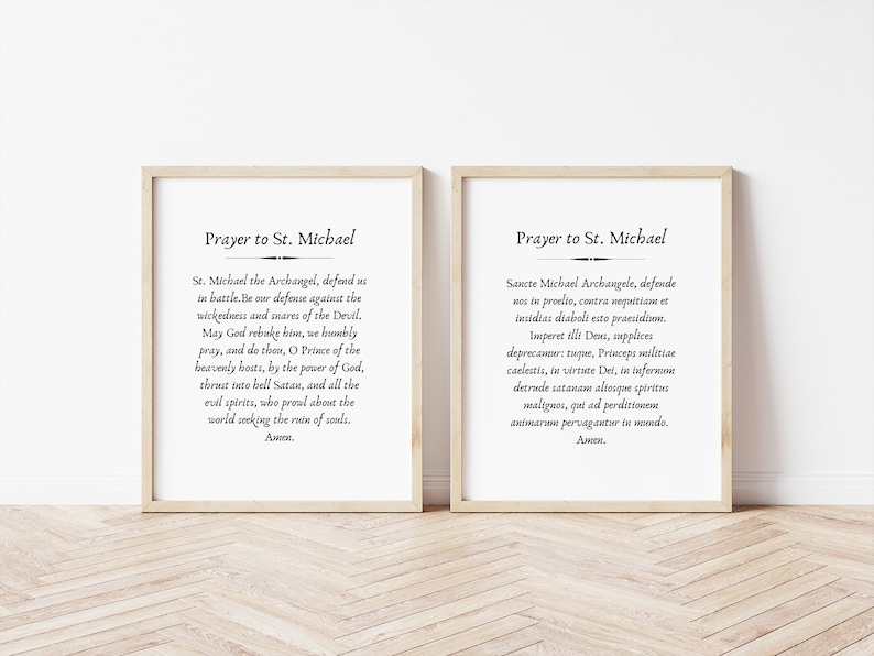 May include: Two framed prints with black text on a white background. The text is a prayer to Saint Michael. The top print reads "Prayer to St. Michael" and the bottom print reads "St. Michael the Archangel, defend us in battle. Be our defense against the wickedness and snares of the Devil. May God rebuke him, we humbly pray, and do thou, O Prince of the heavenly hosts, by the power of God, thrust into hell Satan, and all the evil spirits, who prowl about the world seeking the ruin of souls. Amen."