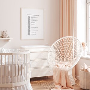 May include: A white crib with a white and gray bedding set, a white dresser, a white chair with a pink blanket, and a framed print of the Ten Commandments on a pink wall.