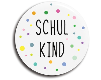 May include: White round button with a colourful polka dot pattern around the edges. The text "SCHUL KIND" is printed in black in the centre of the button.