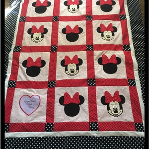 May include: A handmade quilt featuring Minnie Mouse. The quilt has a white background with red polka dot borders and black polka dot edging. Minnie Mouse's face and bow are prominently displayed in the quilt's design.