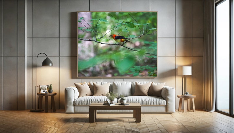 May include: A framed print of a colorful bird perched on a branch in a green forest setting. The bird has a red head, black wings, and a yellow body. The print is displayed on a white wall in a modern living room setting.
