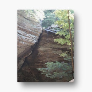 May include: A close-up view of a rock formation in a forest. The rock is brown and has a layered texture. Green trees are visible in the background.