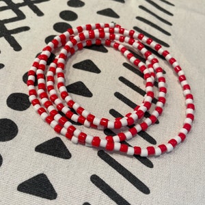 May include: A red and white beaded necklace with multiple strands. The beads are small and round.