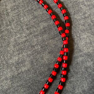 May include: A close-up of a red and black beaded necklace. The necklace is made of small, round beads that are strung together in a repeating pattern.
