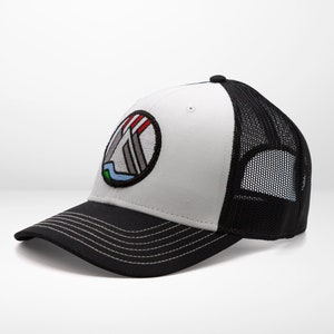 May include: A white and black trucker hat with a colorful logo of a mountain range inside a circle. The logo has red, white, blue, and green accents.