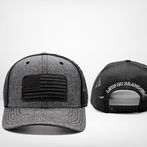 Puede incluir: Una gorra de camionero negra y gris con un parche de la bandera estadounidense negra en la parte delantera y el texto "Let's Go Brandon" bordado en la parte posterior.