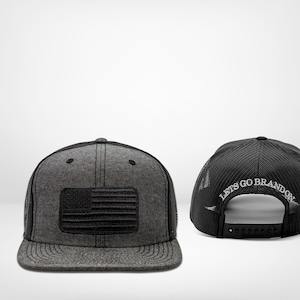 Puede incluir: Una gorra de camionero negra y gris con un parche de la bandera estadounidense negra en la parte delantera y el texto "Let's Go Brandon" bordado en la parte posterior.