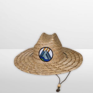 May include: A straw hat with a brown and tan woven design. The hat has a round, flat brim and a tall, pointed crown. A circular patch with a blue, gray, and yellow mountain design is sewn onto the front of the hat.
