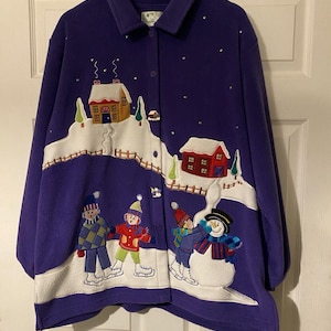 May include: A purple fleece jacket with a winter scene design. The jacket features an embroidered landscape with houses, trees, and figures ice skating. The design includes a snowman and sparkling accents.