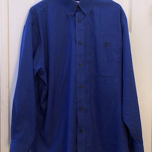 May include: A long-sleeve button-down shirt in a vibrant blue and black micro-check pattern. The shirt features a classic point collar with buttons, a front placket with dark buttons, and a single chest pocket on the left side of the garment.