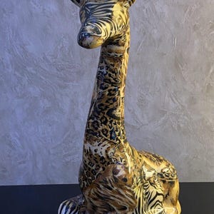May include: A ceramic giraffe figurine featuring a glossy finish with a multi-animal print pattern. The surface displays a combination of black and white zebra stripes, brown and black leopard spots, and tiger-like markings across the entire body.