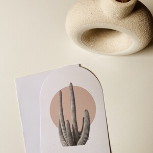 May include: A white card with a rounded arch shape features a graphic of a cactus plant with a pink circle behind it. The cactus is in the center of the card and the pink circle is behind it.