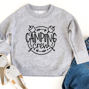 May include: A grey sweatshirt with a black graphic design that says "Camping Crew" with a circle around the text and two crossed sticks with marshmallows on the ends.