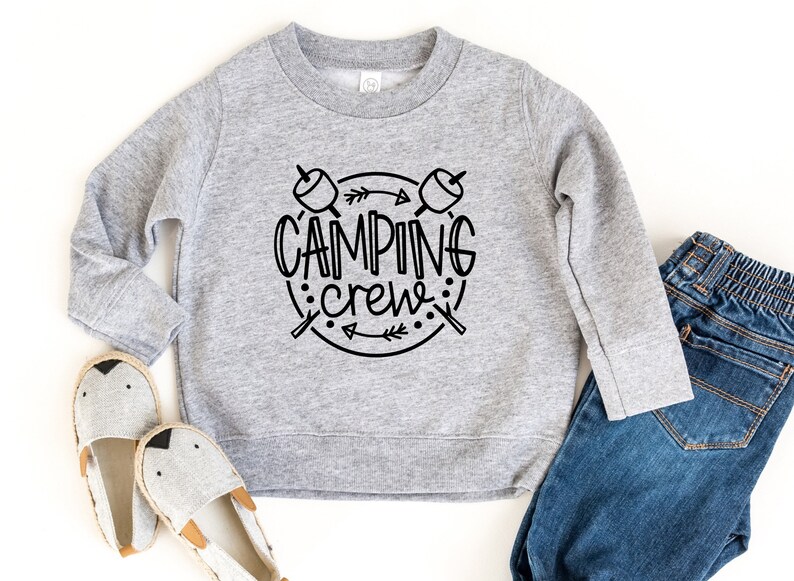 May include: A grey sweatshirt with a black graphic design that says "Camping Crew" with a circle around the text and two crossed sticks with marshmallows on the ends.