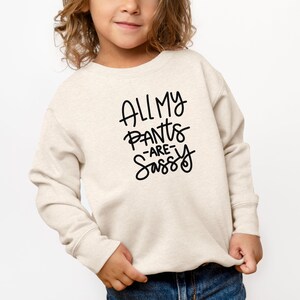 Może przedstawiać: Jasnobeżowa bluza z czarnym nadrukiem "All My Pants Are Sassy".