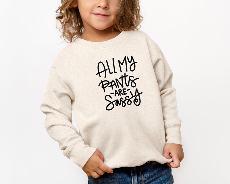 Może przedstawiać: Jasnobeżowa bluza z czarnym nadrukiem "All My Pants Are Sassy".