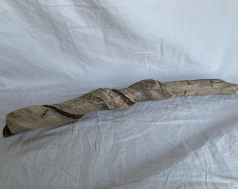 May include: A long, twisted piece of driftwood with a natural, weathered gray finish. The wood has a unique, organic shape and texture.