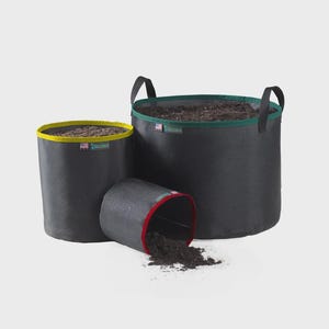 May include: Three black fabric grow bags of varying sizes, filled with soil. The largest has green trim and handles, the medium has yellow trim, and the smallest is tipped over, with red trim. All have soil inside.