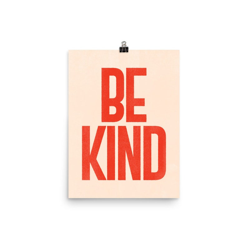 Puede incluir: Un p&oacute;ster beige con el texto "BE KIND" en letras rojas. Las letras son negritas y de bloque.