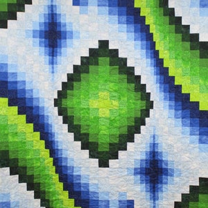 May include: A quilt with a geometric pattern of green, blue, and white squares. The squares are arranged in a diagonal pattern, creating a sense of movement. The quilt is made with a variety of fabrics, including some with a subtle floral pattern.