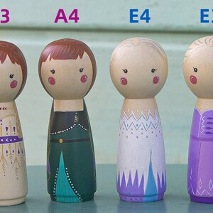 Puede incluir: Cuatro mu&ntilde;ecas de madera de clavija, cada una con un peinado y un vestido diferentes. Las mu&ntilde;ecas est&aacute;n pintadas con detalles intrincados, que incluyen un vestido dorado y morado, un vestido verde y azul, un vestido blanco y morado y un vestido morado con una trenza.