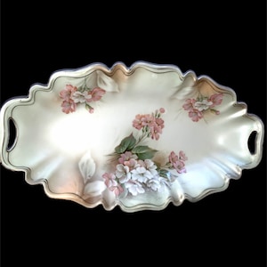 May include: A white oval serving dish with a scalloped edge and two handles. The dish is decorated with a floral pattern in shades of pink and green.