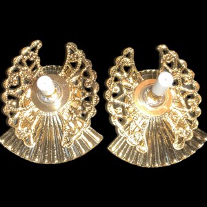 May include: Two gold-colored candle holders with a decorative filigree design and a white candle holder in the center of each.