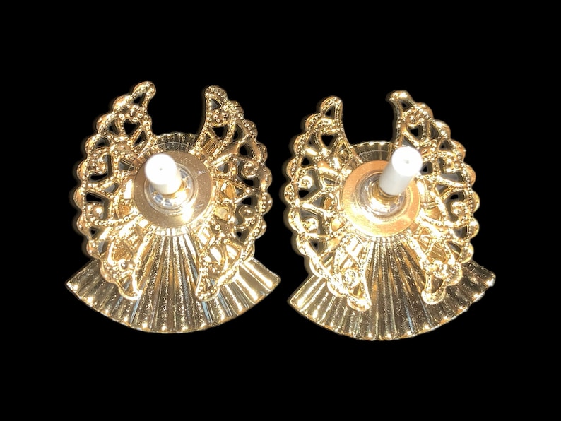 May include: Two gold-colored candle holders with a decorative filigree design and a white candle holder in the center of each.
