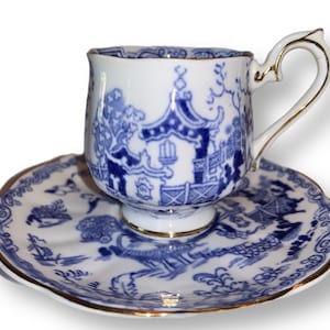 May include: A blue and white porcelain teacup and saucer set with a gold trim. The set features a traditional Chinese design with a pagoda and trees.