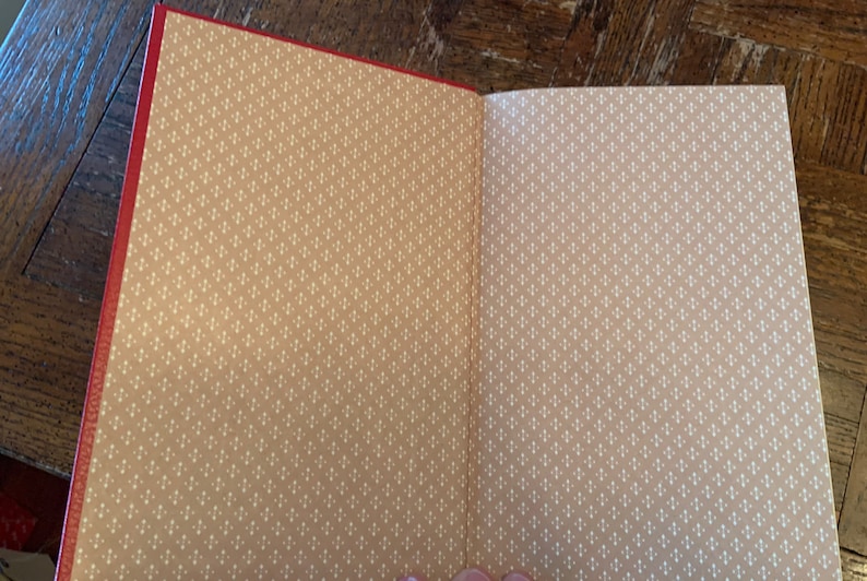 May include: An open book with a red cover and tan pages. The pages have a repeating pattern of small white dots.